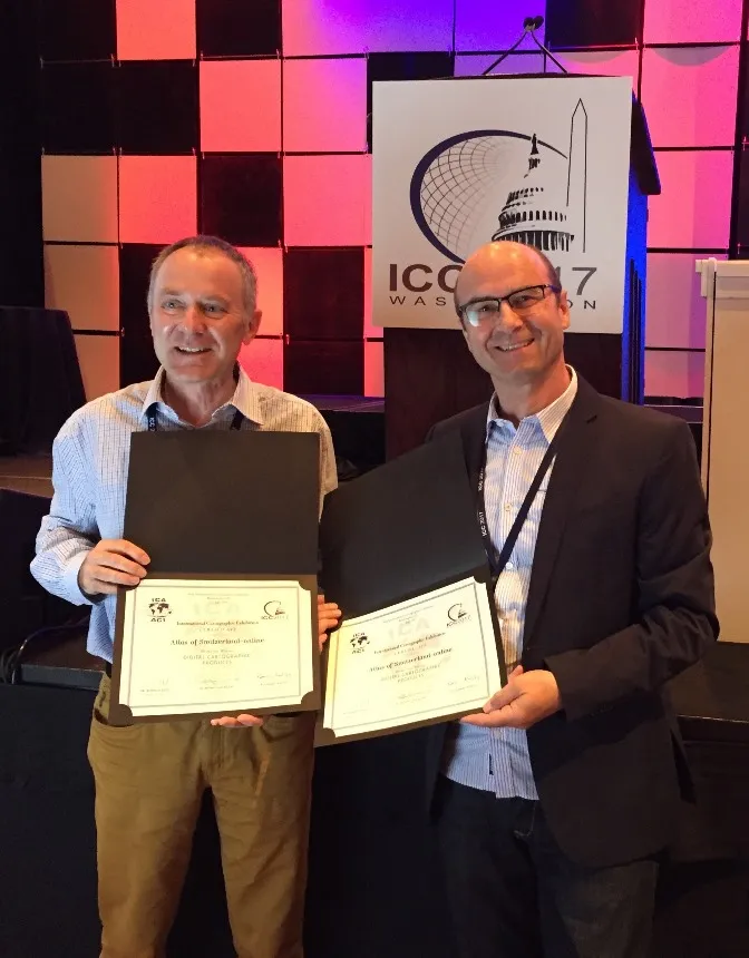 Lorenz Hurni und René Sieber mit den zwei ICA-Auszeichnungen. Zwei lächelnde Männer stehen und halten zwei Auszeichnungen in den Händen.