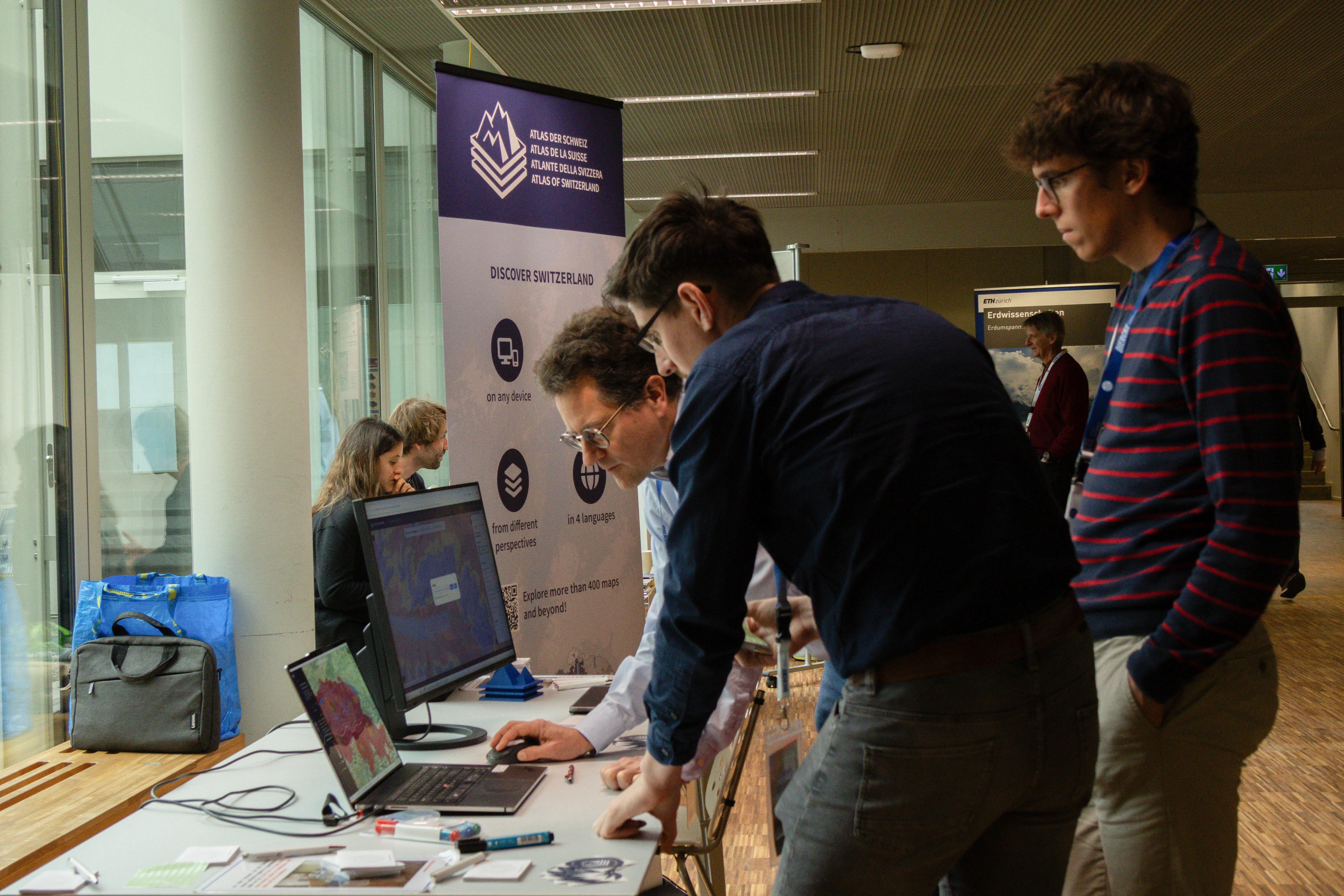 Drei Personen stehen vor einem Computer, auf dessen Bildschirm eine Karte angezeigt wird, und diskutieren darüber.