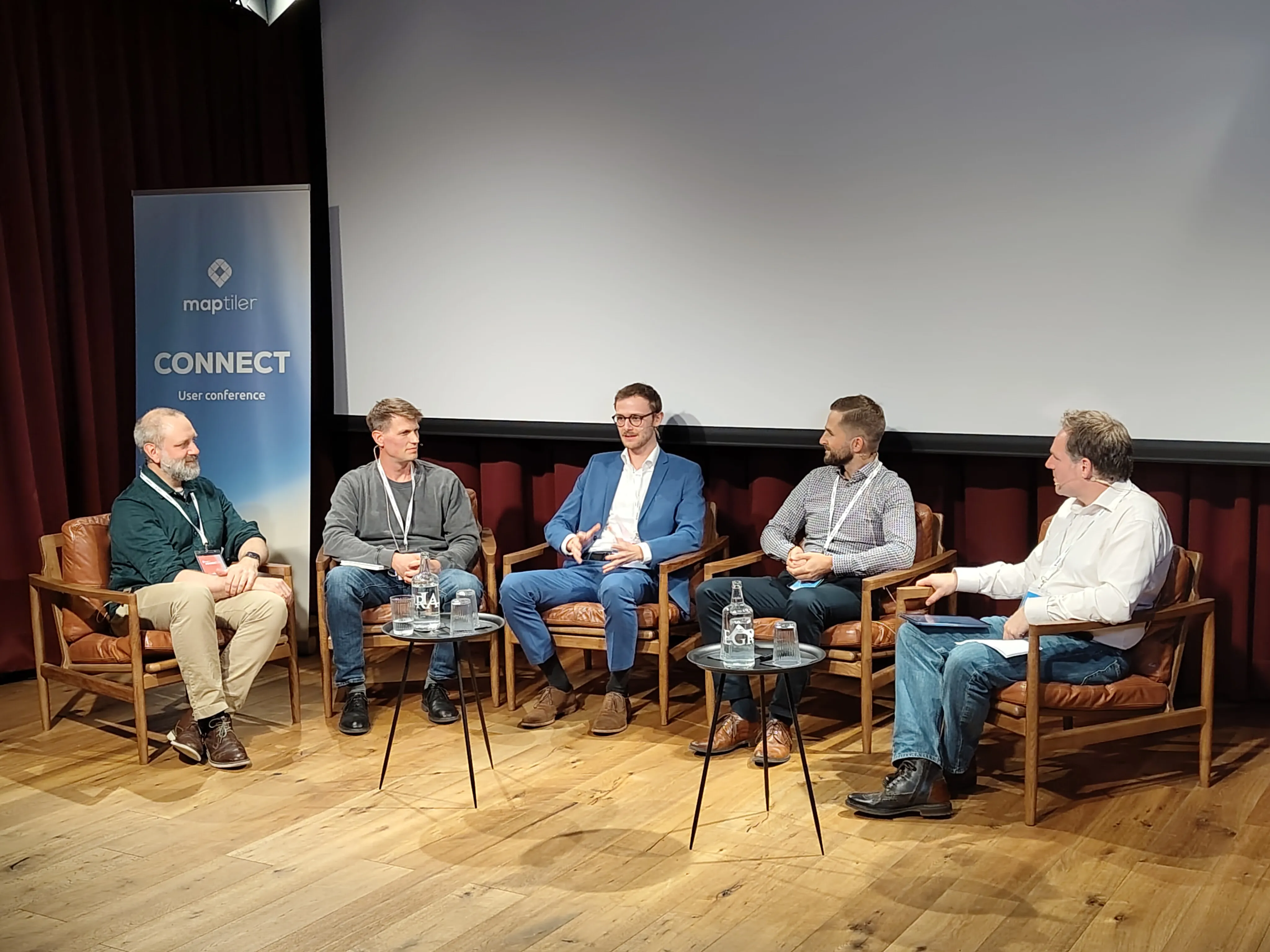 Vier Personen sitzen auf Stühlen auf einer Bühne und diskutieren miteinander.